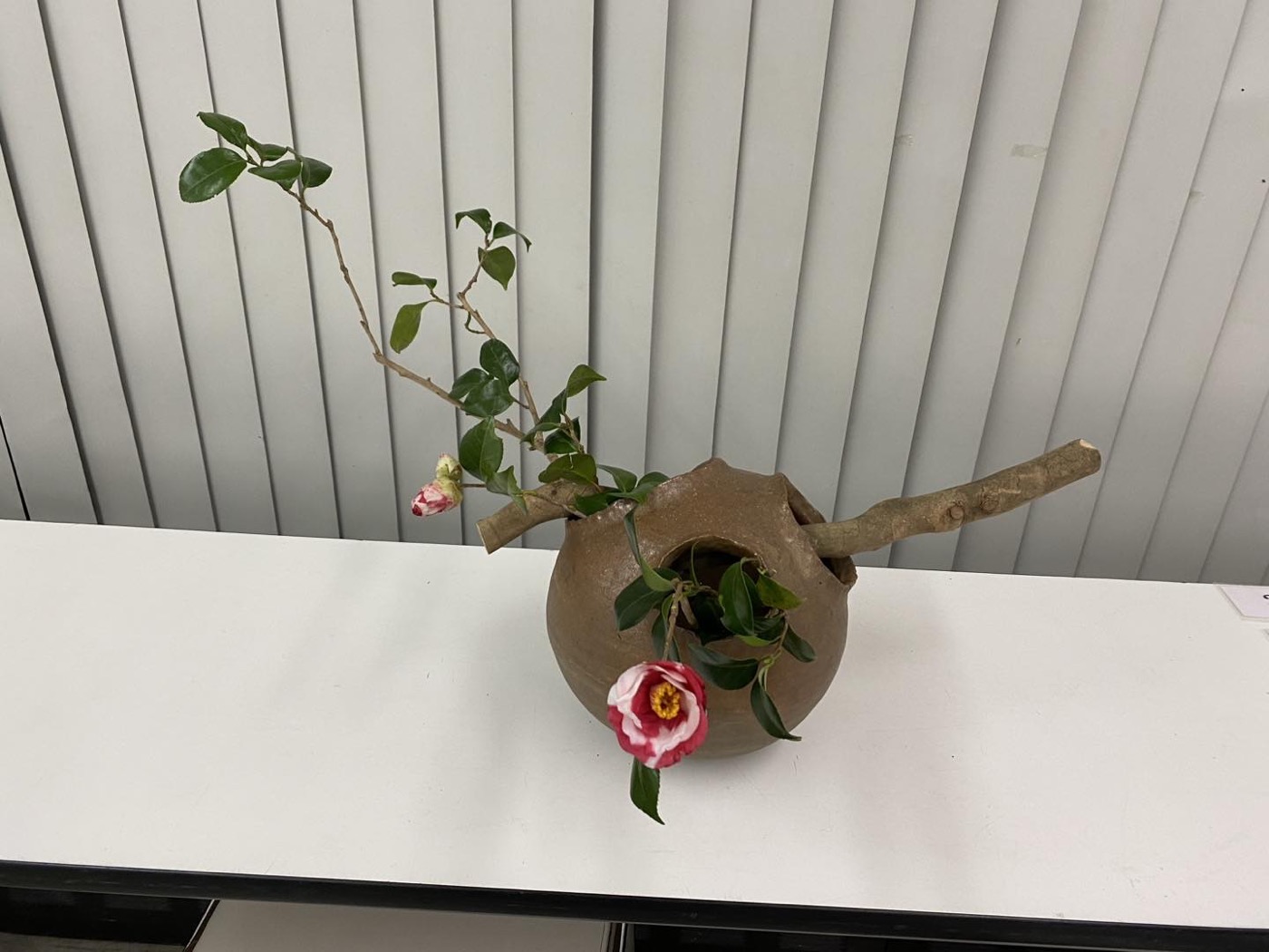 椿と枝を土色の器に生けた小さないけばな作品