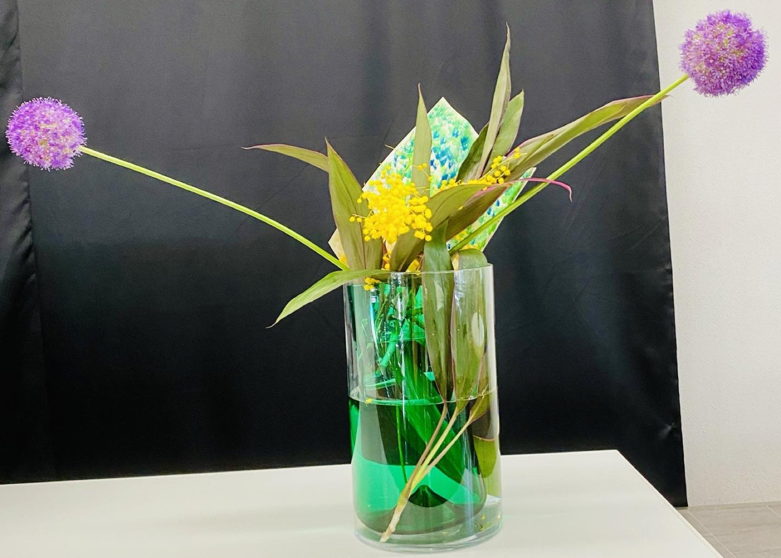 黒い背景の前でガラス器と紫の花を使った現代的ないけばな作品